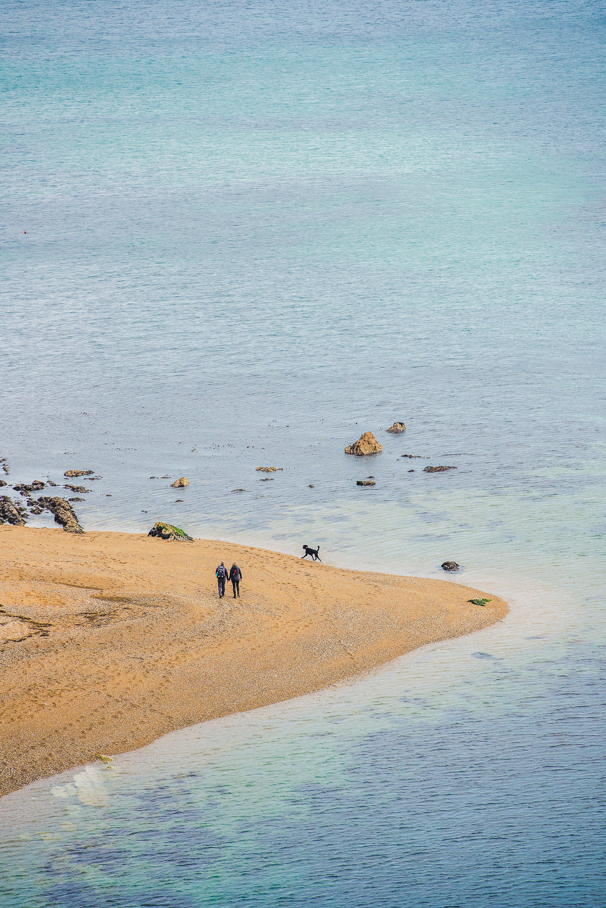 Dog walkers walking round the headland of a pebble beach
