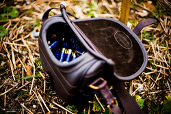 Brown leather shotgun cartridge loader bag. Filled with blue cartridges, on the ground