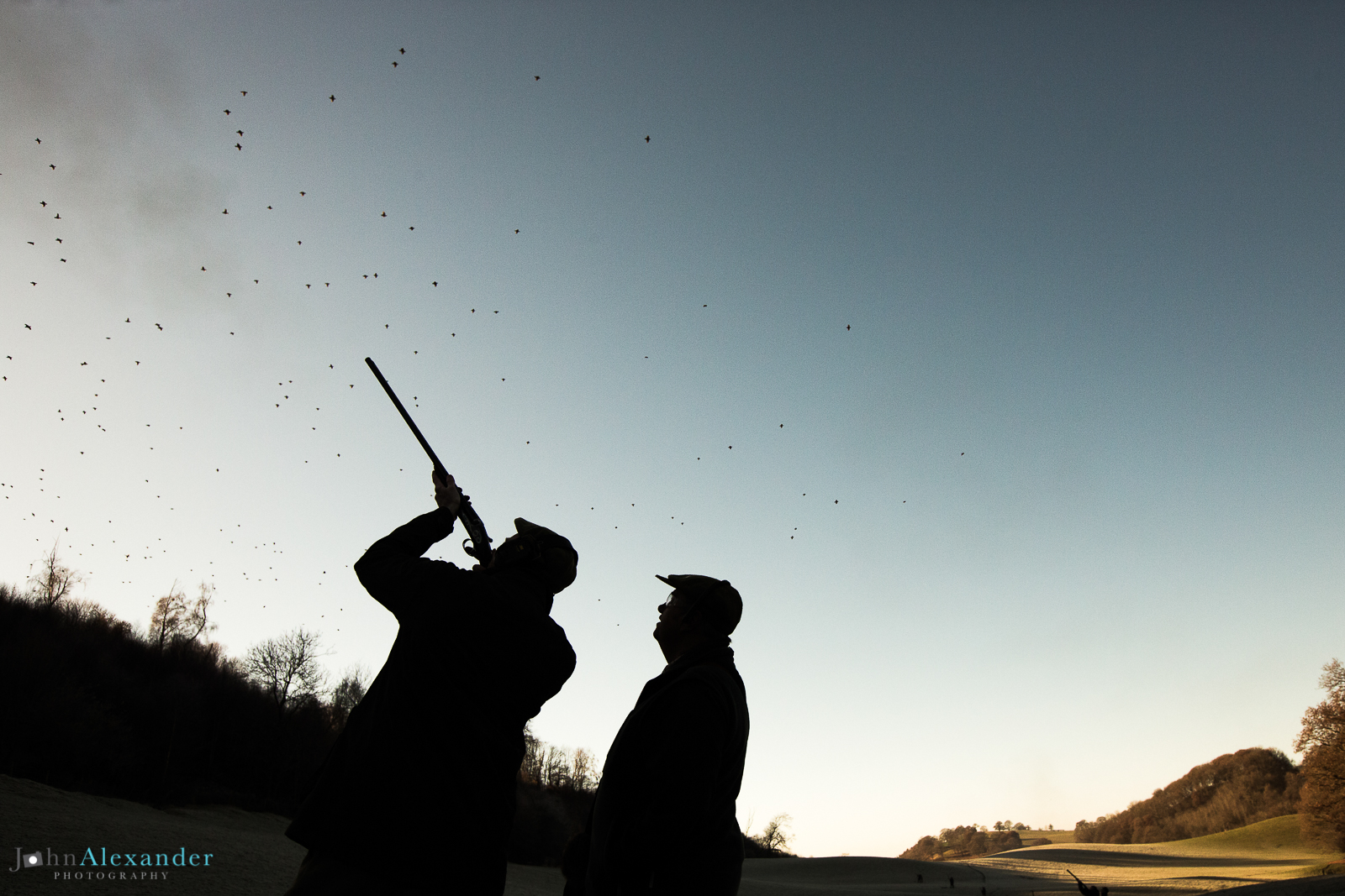 silhouette of a gun and his loader shooting high pheasants in Wales